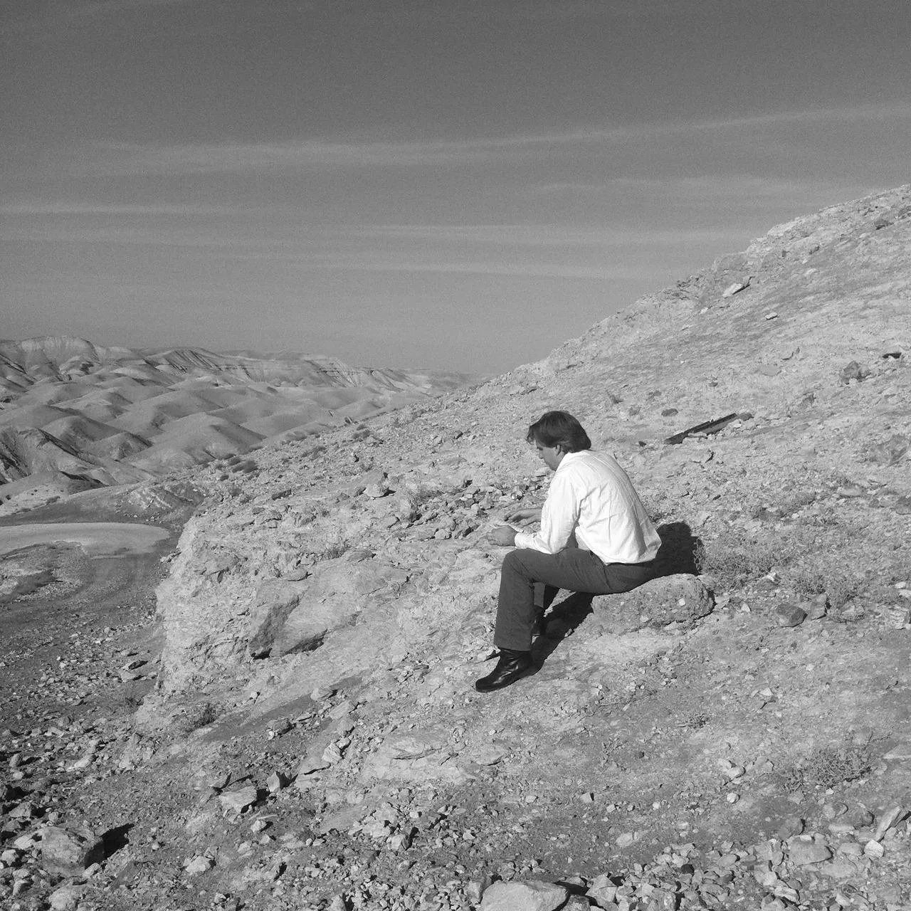 A lone figure seated in a vast rocky landscape